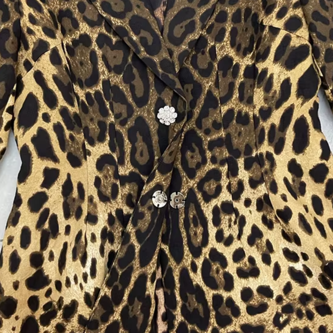 Close-up of a leopard print garment with a tan and black animal pattern, featuring decorative silver-tone flower-shaped buttons on the front.