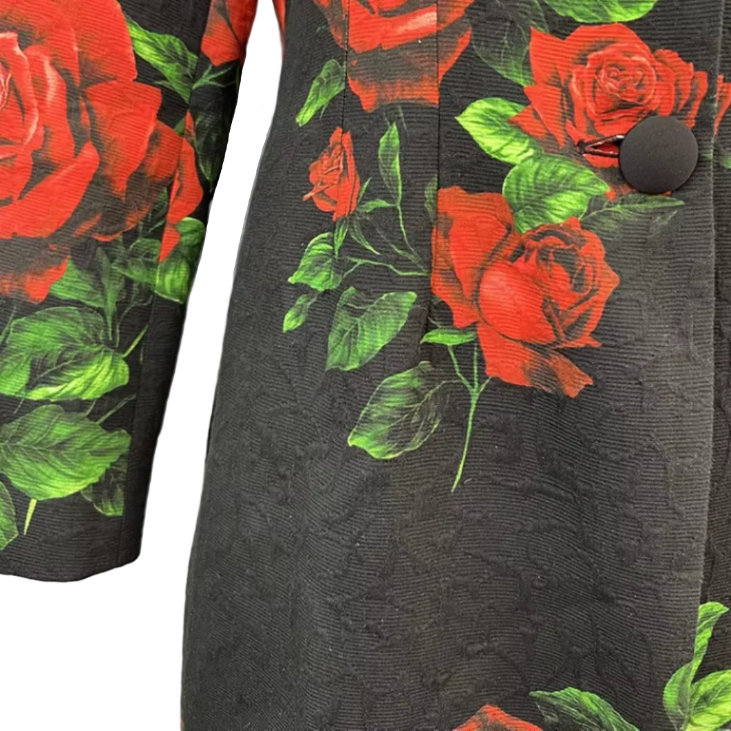Close-up of a black textured fabric garment featuring a bold red rose and green leaf print, with two large black buttons visible.