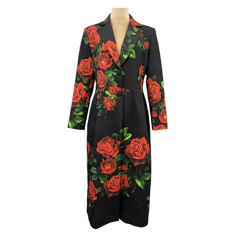 A long black coat with a bold red rose and green leaf print, displayed on a dress form against a gray patterned backdrop.