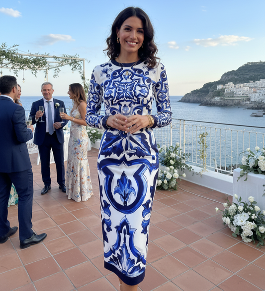 Woman in a blue and white patterned dress standing on a terrace with ocean view